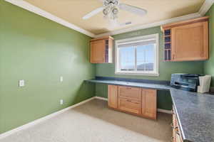 Kitchen with built in study area, dark countertops, ornamental molding, ceiling fan, and open shelves