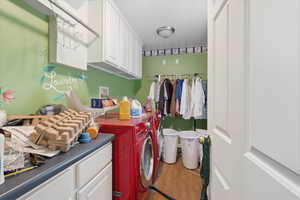 Laundry area with cabinet space, separate washer and dryer, and wood finished floors