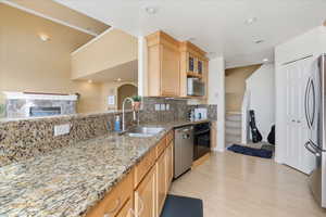 Kitchen with light stone countertops, light wood finish cabinets, tasteful backsplash, stainless steel appliances, and arched walkways