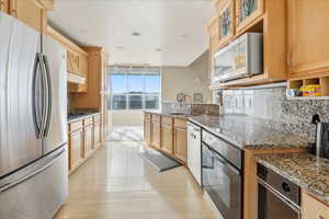 Kitchen with stainless steel appliances, dark stone countertops, decorative backsplash, and light wood finish cabinetry