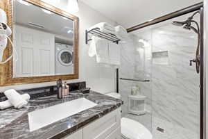 Bathroom featuring washer / clothes dryer, vanity, and a marble finish shower