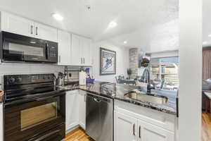 Kitchen featuring black appliances, white cabinetry, dark stone counters, light wood-style floors, and a textured ceiling