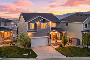 View of front of property featuring a yard, driveway, an attached garage, stone siding, and a storage unit