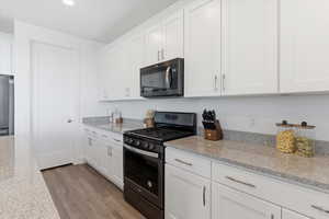 Kitchen with stainless steel appliances, white cabinets, light stone countertops, light wood finished floors, and recessed lighting