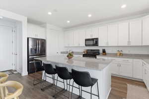 Kitchen featuring stainless steel fridge, dark wood finished floors, black gas range oven, a center island, and light stone counters