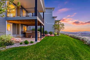 Back of property at dusk with a hot tub, a patio area, a lawn, and a balcony