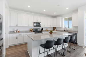 Kitchen with light stone counters, white cabinets, stainless steel appliances, a breakfast bar area, and dark wood-style flooring