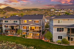Back of house at dusk with a hot tub, a patio, a lawn, a balcony, and a residential view