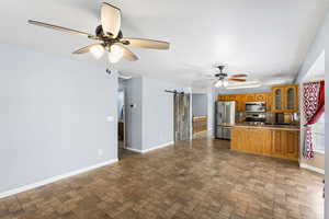 Kitchen with a barn door, ceiling fan, a peninsula, wood finish cabinets, and stainless steel appliances