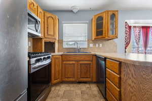 Kitchen featuring stainless steel appliances, glass fronted cabinets, light countertops, and stone finish floors