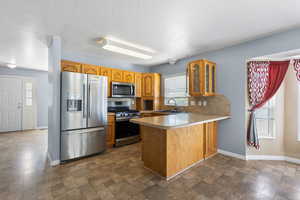 Kitchen featuring a peninsula, stainless steel appliances, glass fronted cabinets, light countertops, and wood finish cabinetry
