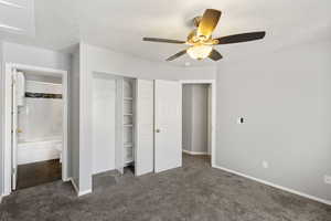 Unfurnished bedroom with dark carpet, a closet, a ceiling fan and an  anattached bathroom