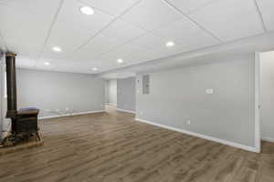Unfurnished living room with a drop ceiling, recessed lighting, a wood stove, wood finished floors, and electric panel