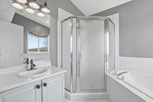 Bathroom with a garden tub, a stall shower, vanity, vaulted ceiling, and light tile patterned flooring