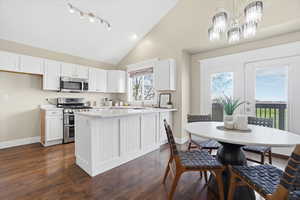 Kitchen with light countertops, white cabinets, stainless steel appliances, a peninsula, and lofted ceiling