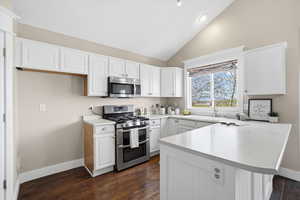Kitchen featuring a peninsula, stainless steel appliances, light countertops, dark wood-style floors, and white cabinetry