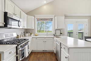 Kitchen featuring stainless steel appliances, a peninsula, white cabinets, lofted ceiling, and dark wood-type flooring