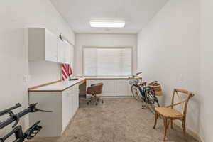 Home office with light colored carpet, built in desk, and a textured ceiling