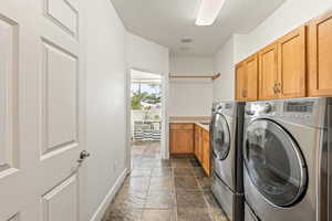 Laundry area with stone tile floors, cabinet space, separate washer and dryer, and a textured ceiling