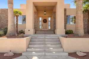 Doorway to property with stucco siding, stone siding, and a porch