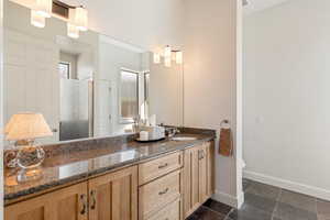 Full bath featuring double vanity, stone tile flooring, and walk in shower