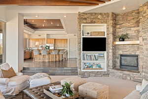 Living room featuring recessed lighting, a stone fireplace, a tray ceiling, ceiling fan, and built in features