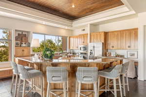 Kitchen featuring a wooden tray ceiling, light stone countertops, stainless steel appliances, a kitchen breakfast bar, and stone tile floors