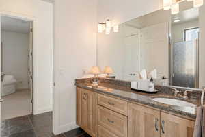 Full bath with double vanity, stone tile flooring, a shower, and a closet