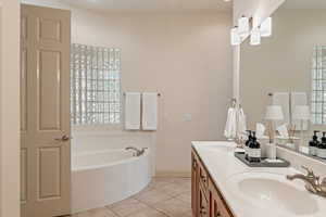 Full bath with double vanity, a bath, and light tile patterned flooring