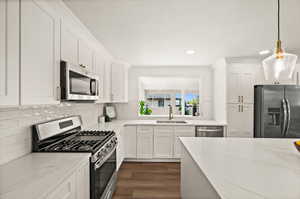 Kitchen with stainless steel appliances, white cabinetry, light stone counters, dark wood-style flooring, and tasteful backsplash