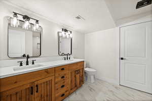 Bathroom with double vanity, a textured ceiling, and light marble finish floors
