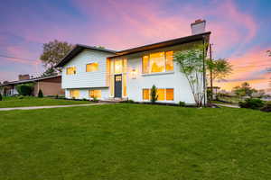 Split foyer home with a chimney, brick siding, and a lawn