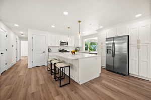 Kitchen with white cabinets, stainless steel appliances, a kitchen island, a kitchen bar, and dark wood-style floors