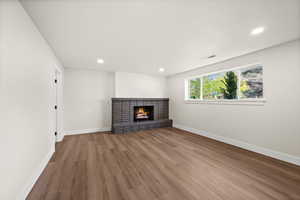 Unfurnished living room featuring wood finished floors, a brick fireplace, and recessed lighting