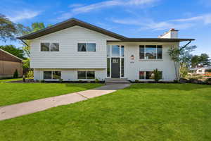 Raised ranch featuring a chimney, a front lawn, and brick siding