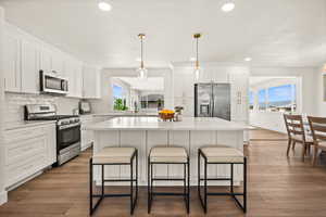Kitchen with stainless steel appliances, white cabinets, a kitchen bar, dark wood-style flooring, and a center island