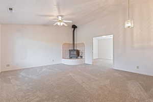 Unfurnished living room featuring lofted ceiling, a wood stove, ceiling fan, and carpet flooring
