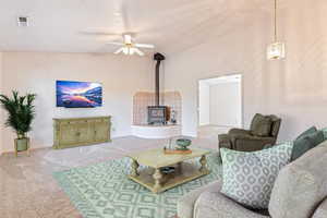 Carpeted living area featuring vaulted ceiling, a wood stove, and ceiling fan
