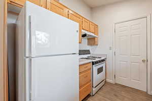 Kitchen featuring white appliances, light countertops, light wood finish cabinetry, and light wood-type flooring