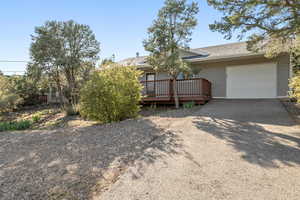 View of front of home featuring driveway, a deck, a garage, and roof with shingles
