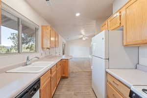 Kitchen with light wood finish cabinetry, light countertops, white appliances, vaulted ceiling, and open floor plan