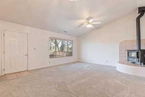 Unfurnished living room featuring a wood stove, a ceiling fan, light carpet, and lofted ceiling