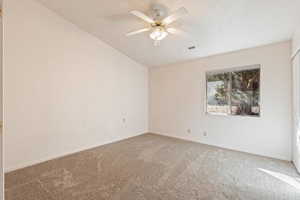 Carpeted empty room featuring a ceiling fan and lofted ceiling