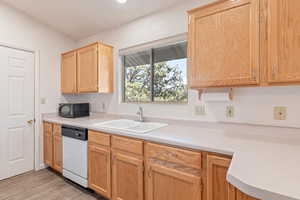 Kitchen with light countertops, black microwave, dishwasher, light wood finish cabinets, and light wood-style flooring