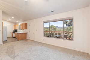 Kitchen featuring lofted ceiling, light countertops, healthy amount of natural light, white appliances, and light colored carpet