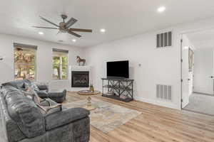 Living area with light wood finished floors, a ceiling fan, a glass covered fireplace, and recessed lighting
