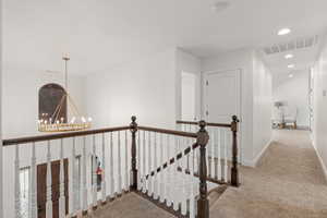 Corridor with an upstairs landing, a chandelier, and light carpet