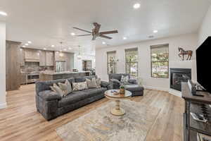 Living area featuring a ceiling fan, a glass covered fireplace, light wood-type flooring, and recessed lighting