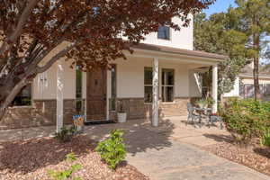 Doorway to property featuring stucco siding, stone siding, and covered porch