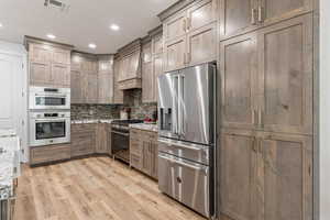 Kitchen with premium appliances, light stone counters, decorative backsplash, light wood-type flooring, and recessed lighting